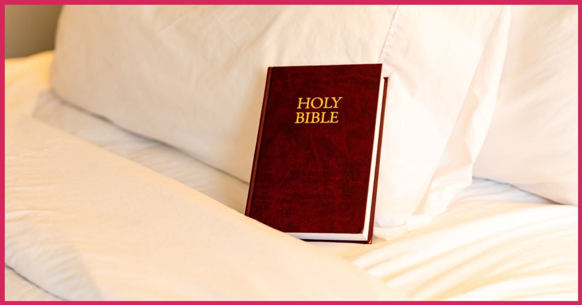 The holy bible sitting on a hotel bed propped up by a pillow