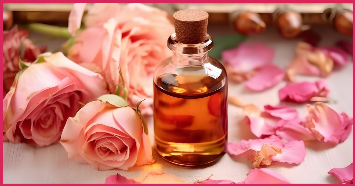 Bottle of rose oil fragrance with pink petals and roses in soft focus background.