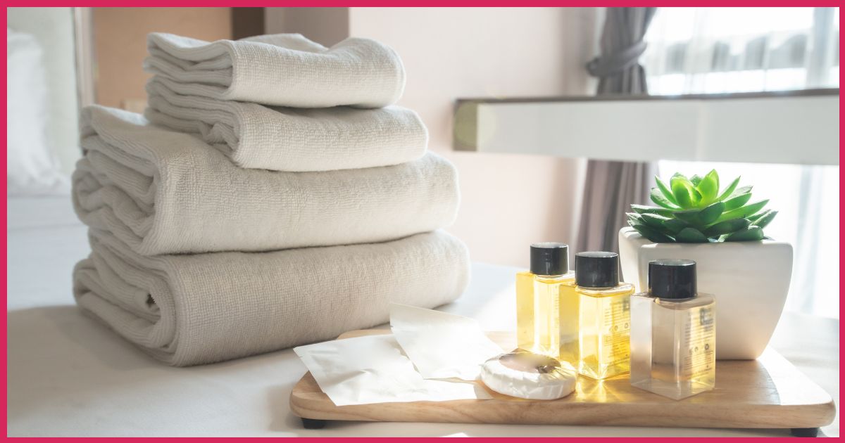 Stack of clean white towels with bottles of toiletries and a green succulent on a wooden tray.