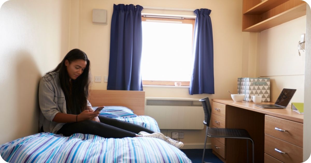 Women sitting on her new student bed, texting on her phone